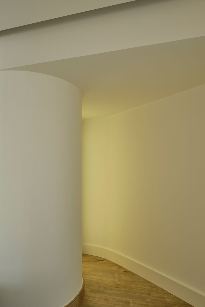 Muro curvo blanco con luz cálida en el apartamento Calasanz