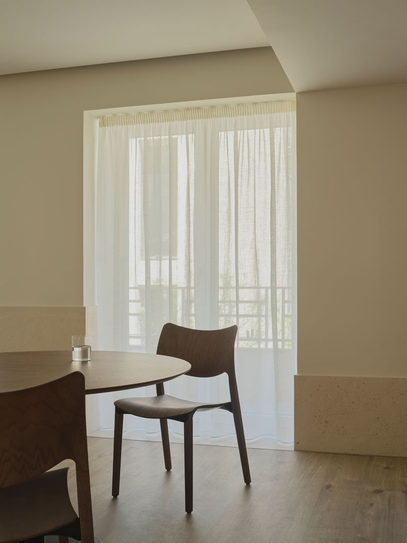 Mesa y silla de madera junto a una ventana con cortinas en el apartamento Calasanz