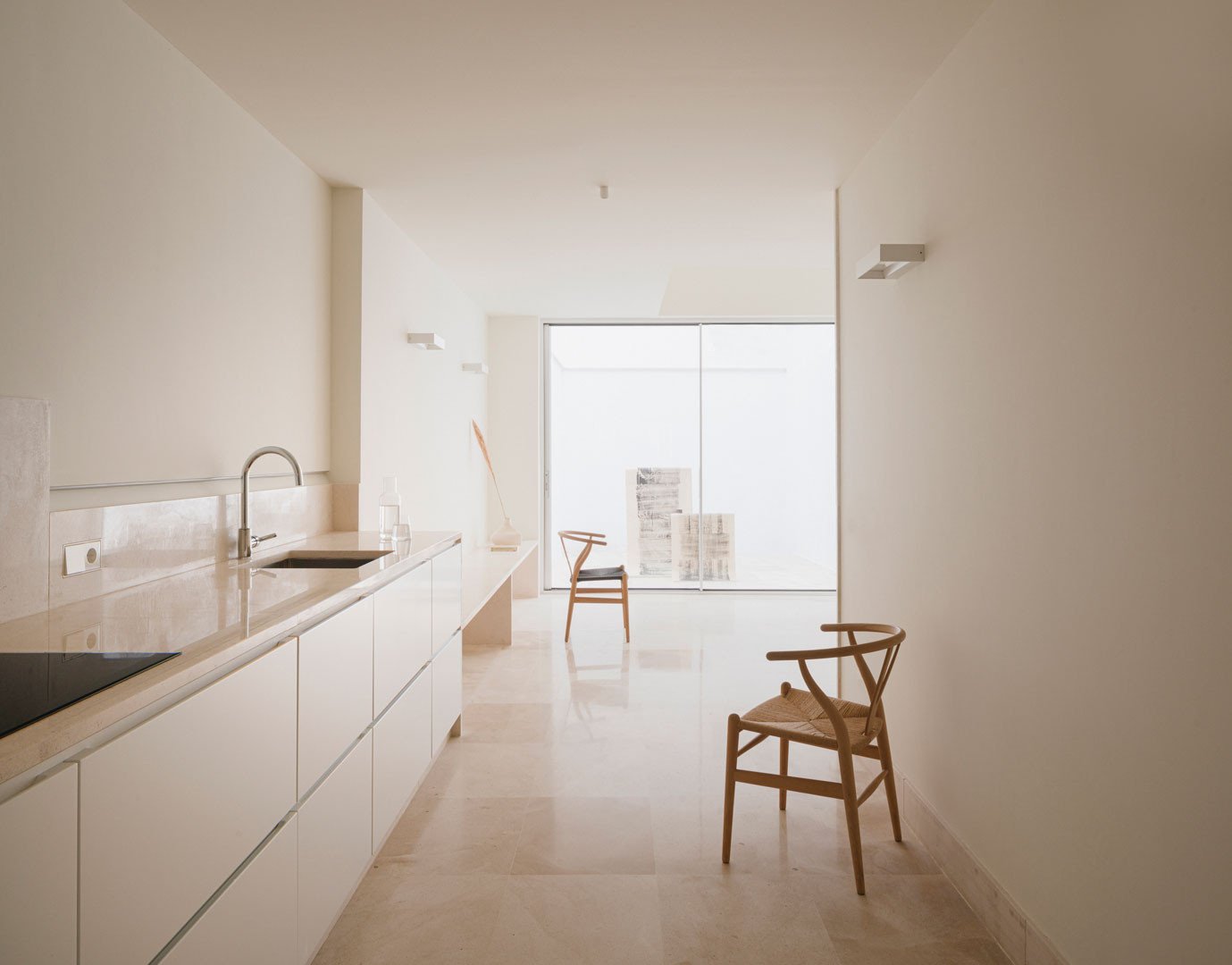 Cocina y estancia continua de planta baja de Casa Mirasol, con encimera de piedra y silla de madera
