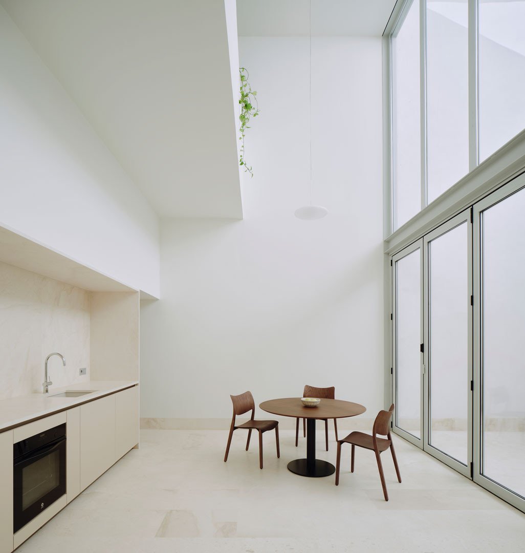 Cocina y comedor en doble altura de Casa Nido, con el ventanal abierto al patio