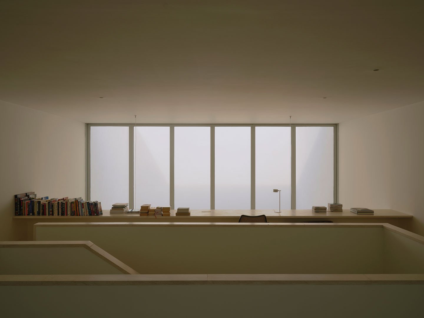 Sala de la planta superior de Casa Nido con ventanal y estanterías sobre el vacío
