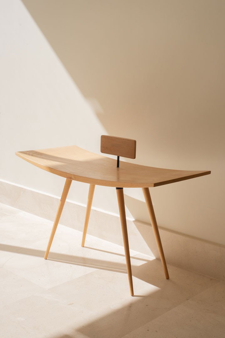 Silla Comba en madera maciza curvada, con respaldo de tablero y patas finas, vista en tres cuartos