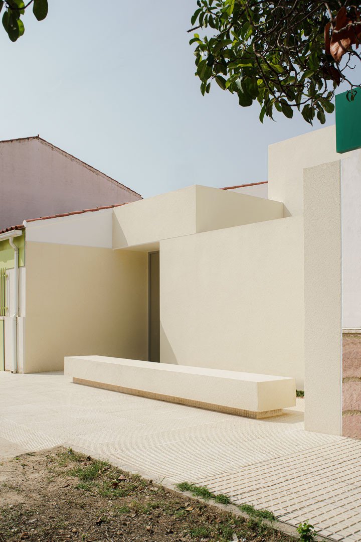 Banco en la línea de calle y volumen blanco de acceso a la Escuela en Aguas Nuevas